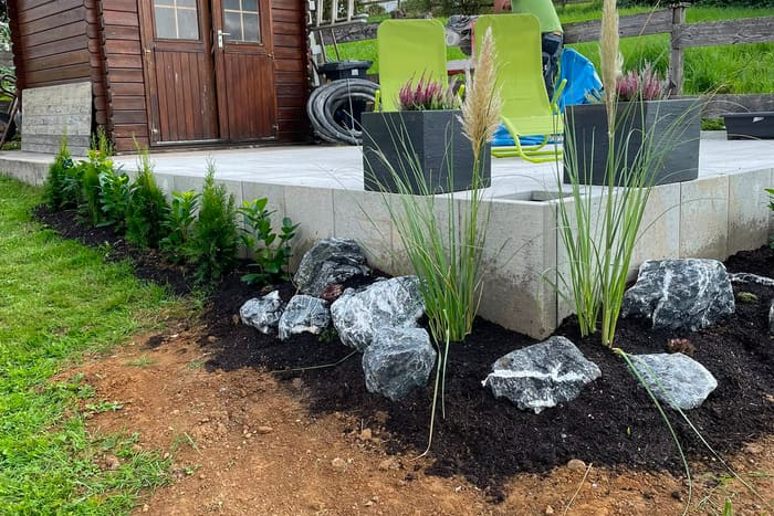 Neu angelegtes Beet mit Ziergräsern, Stauden und Natursteinen an einer Terrassenmauer